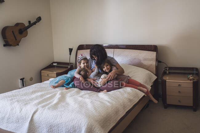 MId-30's mom nursing baby on bed and hugging 4- and 6-yr old daughters — Stock Photo
