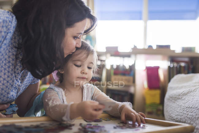 Mid-30's mom kissing head of 4 yr old daughter putting puzzle together — Stock Photo