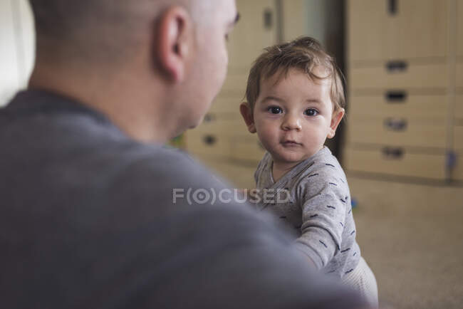 1 year old boy with brown eyes looking past dad 's shoulder — стоковое фото