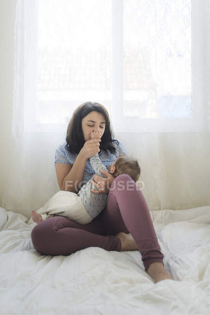 Mãe de meados de 30 com os olhos fechados beijando a mão do bebê enquanto amamenta — Fotografia de Stock