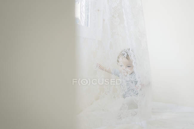 Criança de ano atrás da cortina de renda branca — Fotografia de Stock