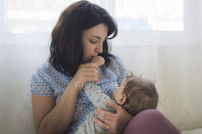 Tierna madre cariñosa besando la mano del bebé mientras amamanta - foto de stock