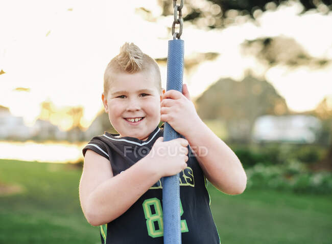 Giovane ragazzo che gioca sull'altalena al parco al tramonto — Foto stock
