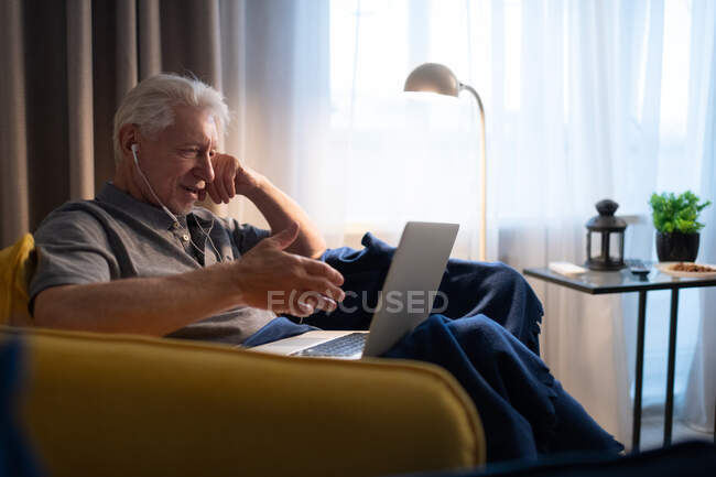 Uomo anziano che riposa in poltrona e fa videochiamate alla famiglia a casa — Foto stock