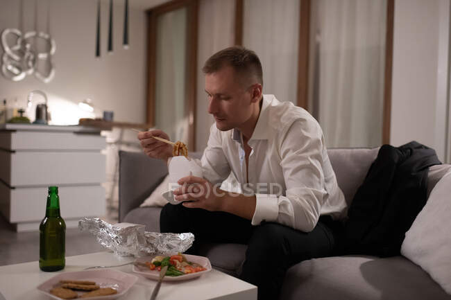Adulti manager maschio mangiare tagliatelle consegna durante il riposo dopo il lavoro a casa — Foto stock