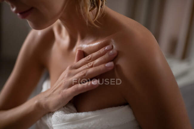 Mulher anônima em creme de manchas de toalha no ombro durante a rotina de cuidados com a pele — Fotografia de Stock