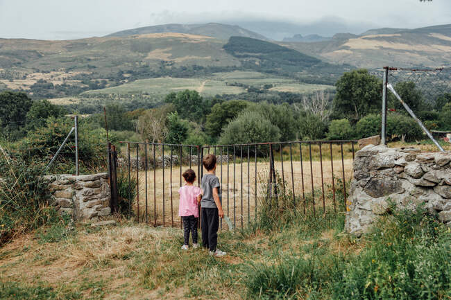 Niños de pie cerca de la valla en el campo montañoso - foto de stock
