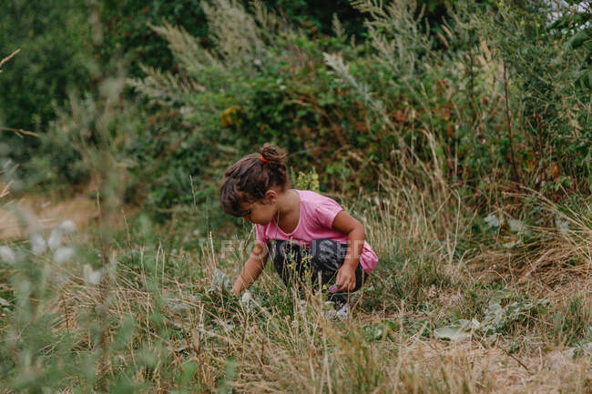 Menina sentada no meio do campo pegando grama — Fotografia de Stock