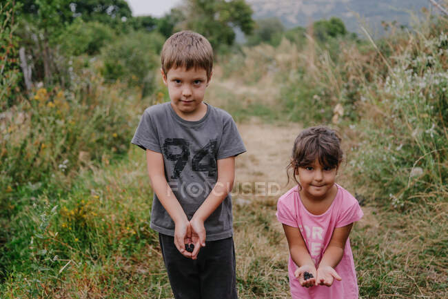 Niños pequeños con bayas en las manos de pie en el bosque - foto de stock
