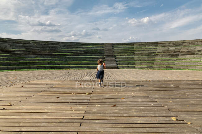 Bambino anonimo con giocattolo in piedi su un'arena di legno vuota — Foto stock