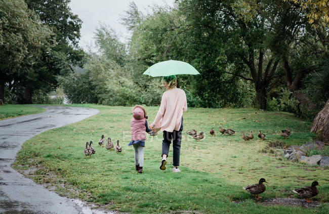 Madre e hija caminando juntas cogidas de la mano en un día lluvioso - foto de stock