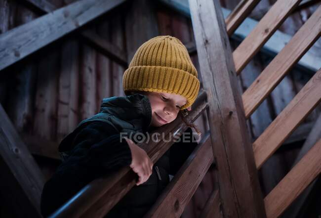 Kleiner Junge auf einer Holztreppe, der durch das schöne Licht nach unten blickt — Stockfoto