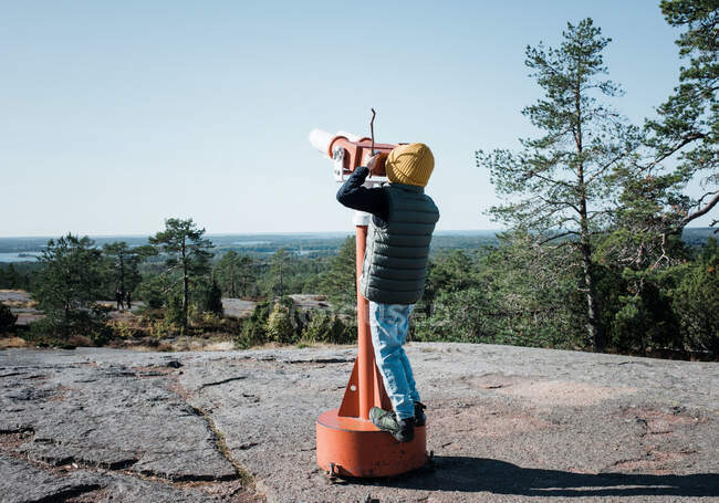 Young boy looking through giant binoculars at a beautiful view — Stock Photo