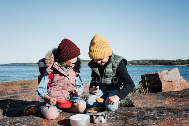 Siblings hiking cooking food on a travel cooker on a sunny day — Stock Photo