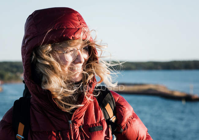 Mujer de pie junto al mar con su pelo soplando en el viento mirando feliz - foto de stock
