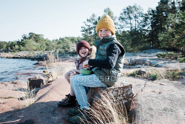 Siblings sat on a rock whilst hiking eating their lunch laughing — Stock Photo