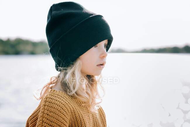 Little girl with curly hair in a cap on lake — Stock Photo