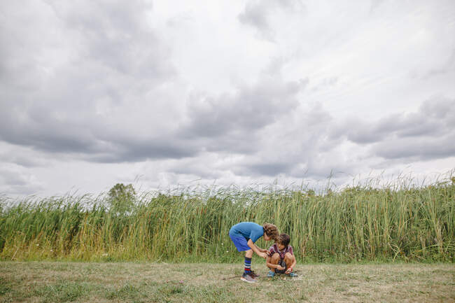 Two boys play together by tall cattails on a cloudy day — Stock Photo