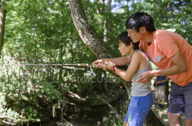 A father reaches out to help hold his son's fishing rod steady — Stock Photo