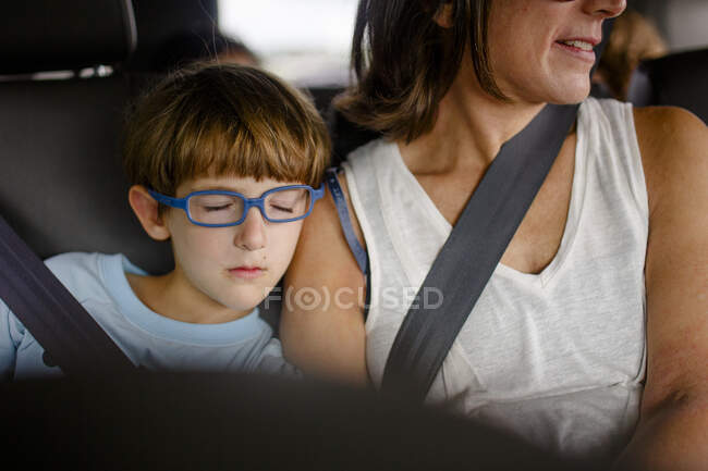 Un bambino piccolo con gli occhiali blu dorme sulla spalla della madre in macchina — Foto stock