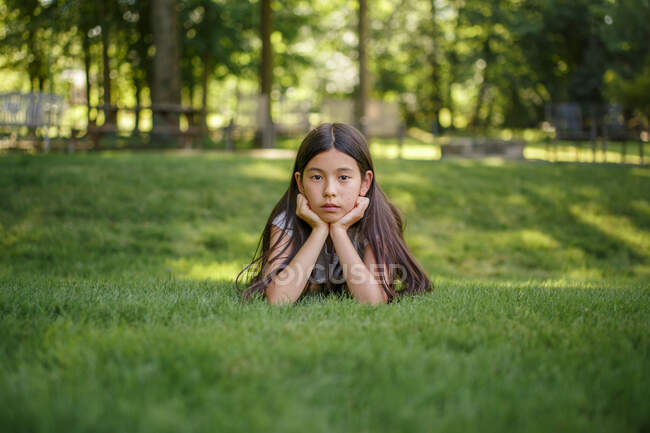 Una chica adolescente yace en la hierba con la cabeza apoyada en sus manos - foto de stock
