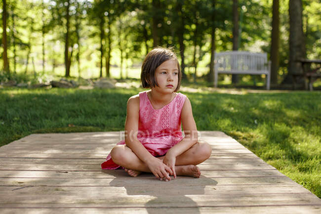 Uma criança séria senta-se em uma ponte de madeira na floresta no verão — Fotografia de Stock
