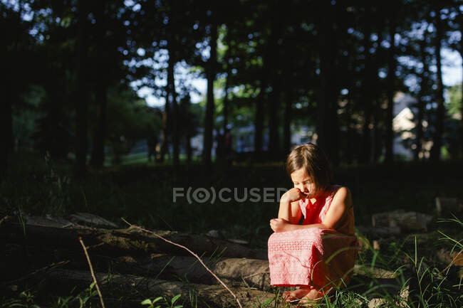 Ein kleines verlassenes Kind sitzt im Sonnenlicht in einem schattigen Waldstück — Stockfoto
