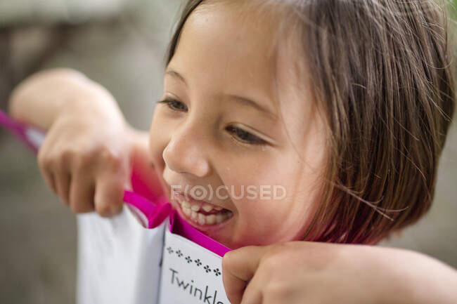 Primer plano de una niña sonriente y alegre sosteniendo orgullosamente un libro - foto de stock