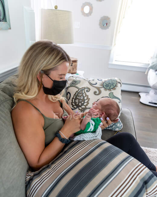 Blonde Frau mit Gesichtsmaske hält neugeborenes Baby. — Stockfoto