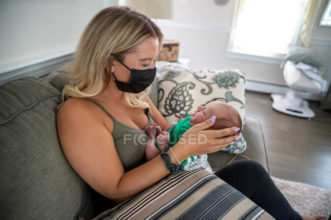 Blonde Frau mit Gesichtsmaske hält schläfriges Neugeborenes. — Stockfoto