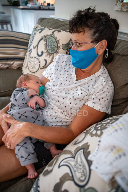 Frau mit Gesichtsmaske hält ihren Enkel. — Stockfoto