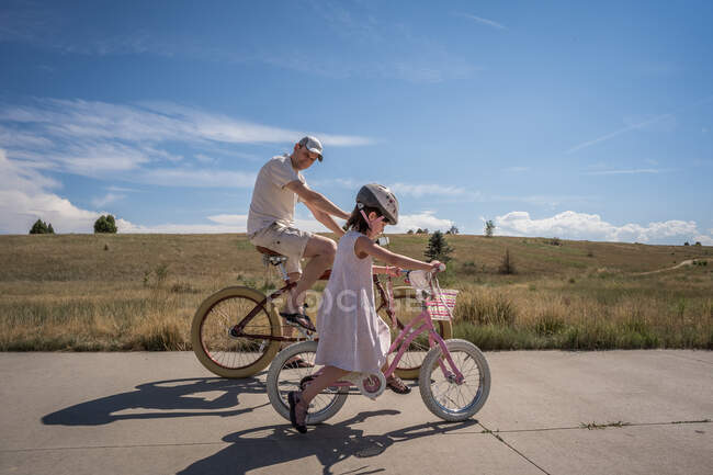 Pai olha para a filha como ela aprende a andar de bicicleta sem treinadores — Fotografia de Stock