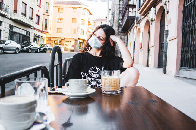 Menina tomando um café no terraço de um bar com uma máscara — Fotografia de Stock