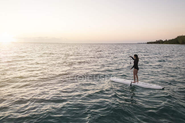 Frau paddelt bei Sonnenuntergang auf See gegen den Himmel — Stockfoto