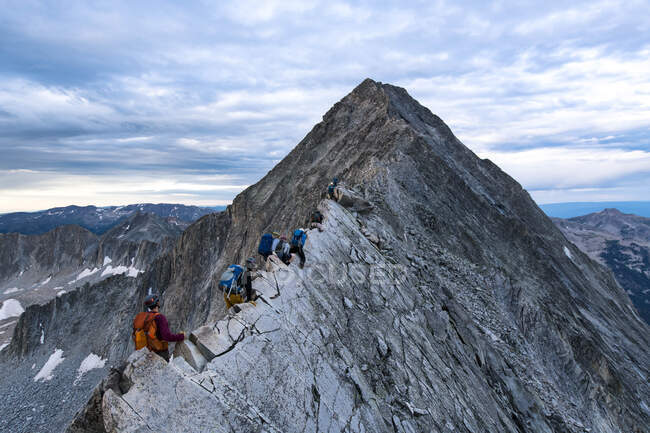 Senderistas masculinos y femeninos escalando el pico de montaña contra el cielo nublado - foto de stock