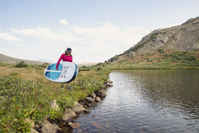 Woman carrying paddleboard at lakeshore against sky — Stock Photo