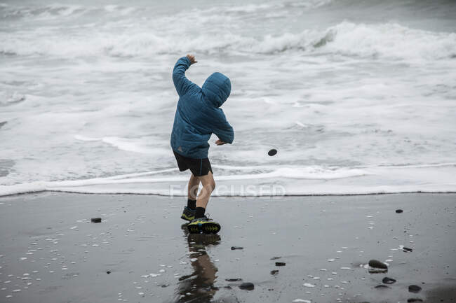 Niño saltando rocas en el Océano Pacífico - foto de stock