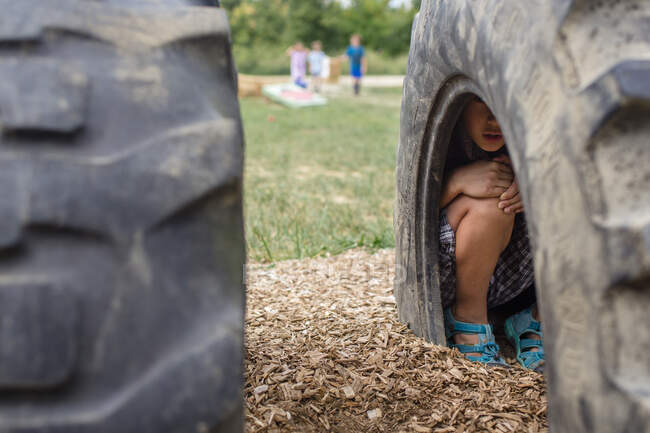 Un chico se mete dentro de un neumático en un patio de recreo en un juego de escondite - foto de stock