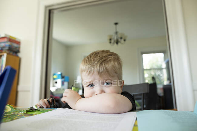 Rubia preescolar niño sentado y haciendo pucheros con barbilla descansando en el brazo - foto de stock
