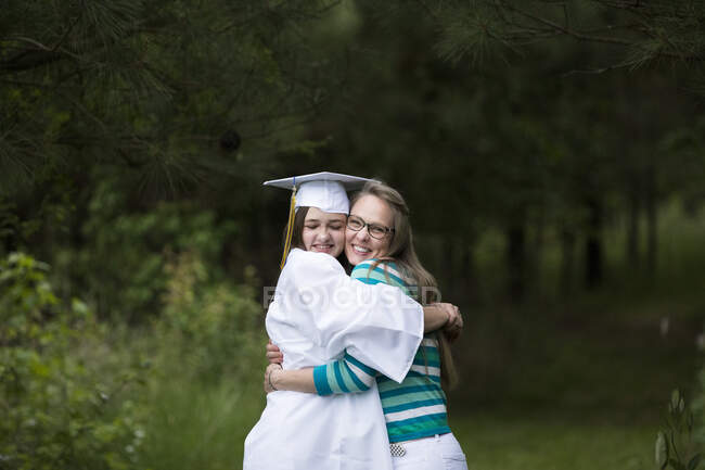 Felice donna laureata indossare cappello bianco e abito stretto abbraccia sua madre — Foto stock