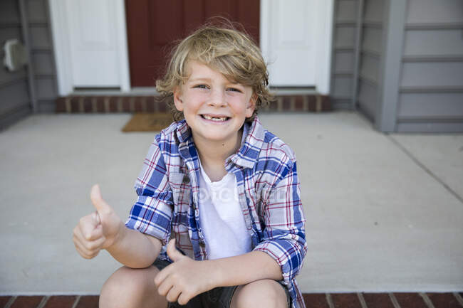 Sans dents première année garçon donne pouce vers le haut tandis que assis sur brique marches — Photo de stock