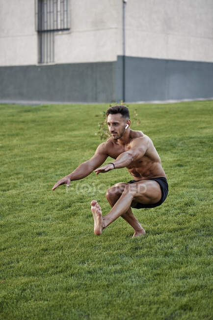 Мужчина без рубашки, занимающийся твёрдой гимнастикой на траве. Калистеническая концепция — стоковое фото
