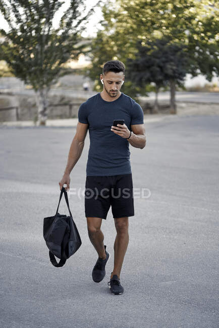An athletic young man walking with a mobile phone in his hand. Calisthenic concept — Stock Photo
