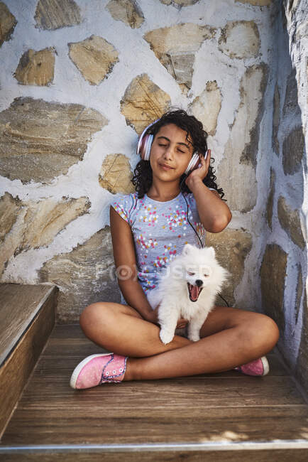 A little girl listens to music with her white dog. Dog concept — Stock Photo