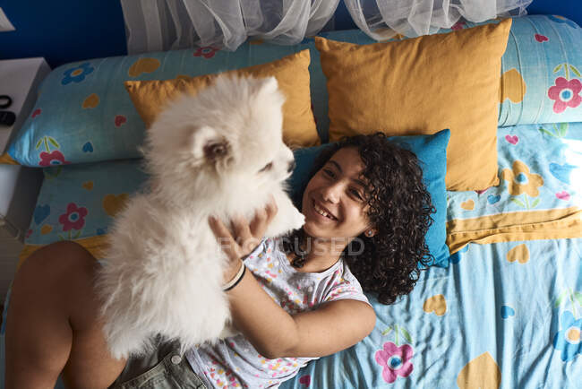 Ein kleines Mädchen spielt mit ihrem weißen Pommernwelpen im Bett. Haustierkonzept — Stockfoto