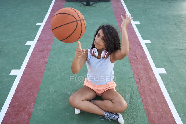 A little girl sitting down spins a basket ball. Lifestyle concept — Stock Photo