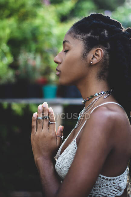 Vista de perfil de una joven afro con las manos juntas en oración - foto de stock