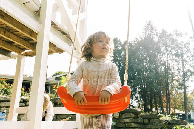 Petite fille tout-petit tenant à son balançoire et détournant les yeux — Photo de stock