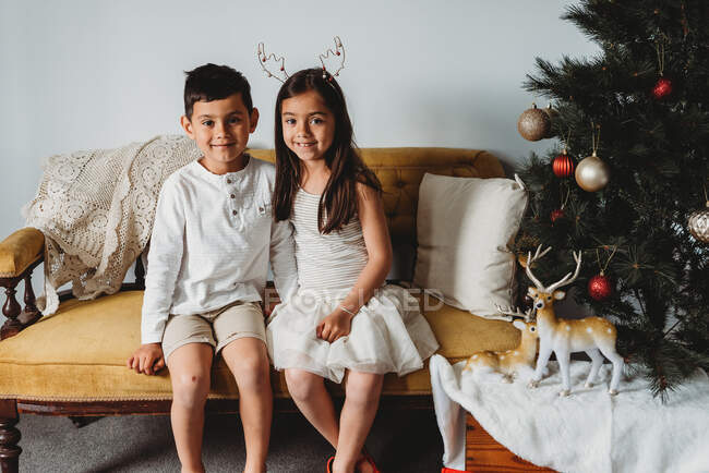 Multiracial young girl & boy sitting on couch next to christmas decor — Stock Photo