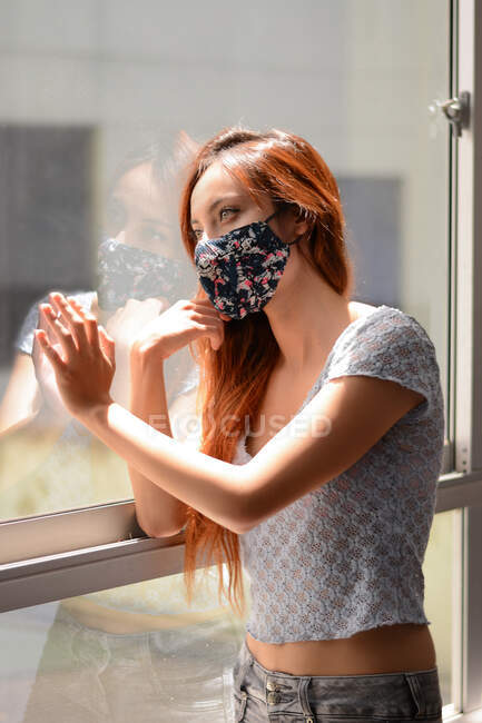 Redhead girl looking through the window at quarantine time — Stock Photo